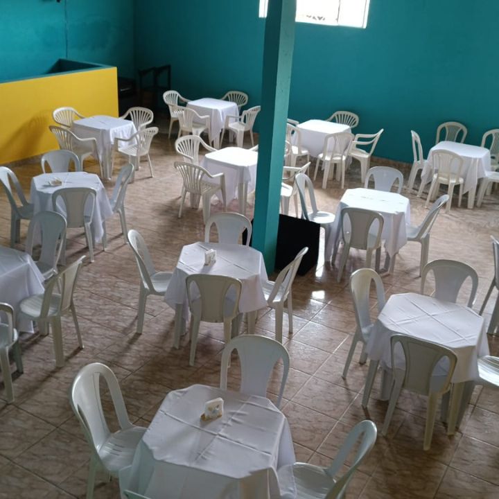 Salão com mesas de toalhas brancas e cadeiras brancas montadas para evento