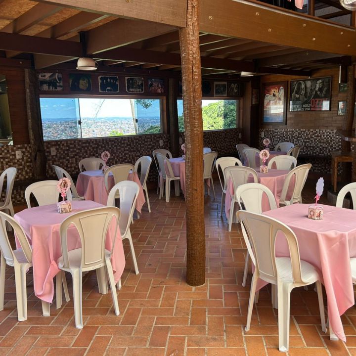 Mesas com toalhas rosa e cadeiras brancas em espaço de festa com vista para a cidade